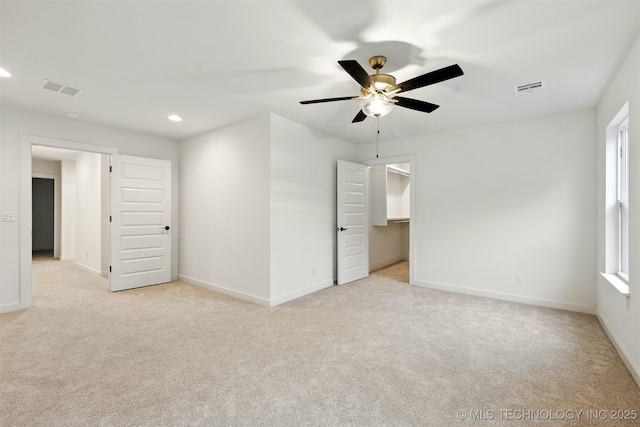 unfurnished bedroom featuring light carpet, recessed lighting, baseboards, ceiling fan, and a walk in closet