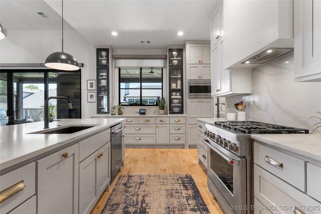 6038 E 119th Pl, Tulsa, OK 74137 - kitchen featuring stainless steel appliances, wall chimney exhaust hood, light wood-style floors, pendant lighting, and glass insert cabinets