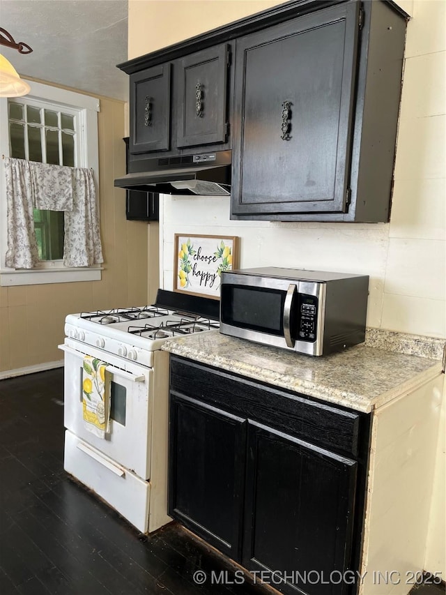 918 W Cedar St, Durant, OK 74701 - kitchen with white gas stove, stainless steel microwave, under cabinet range hood, dark wood finished floors, and dark cabinetry