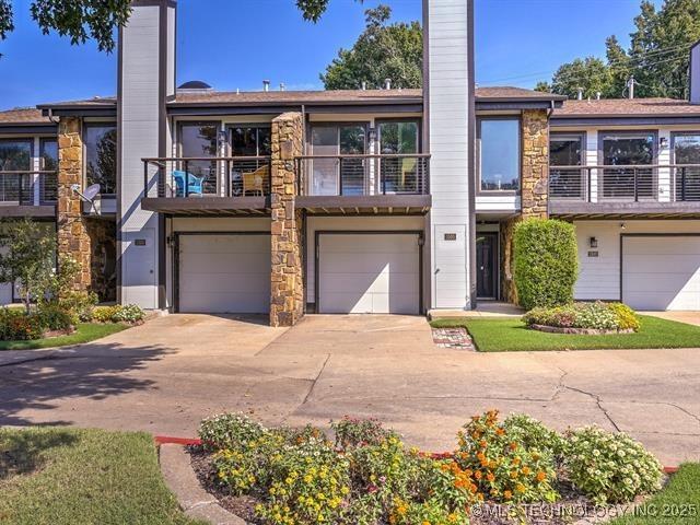multi unit property with a chimney, a garage, driveway, a balcony, and stone siding