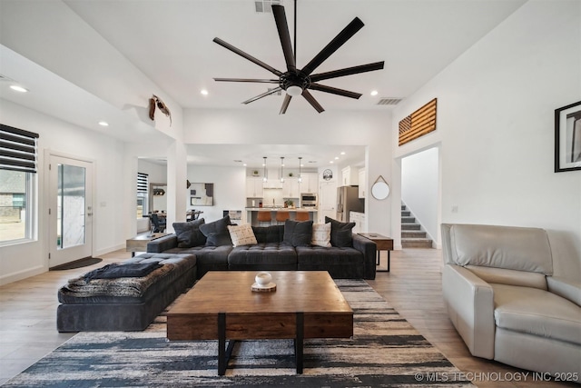 living area with light wood-type flooring, a ceiling fan, stairs, and recessed lighting