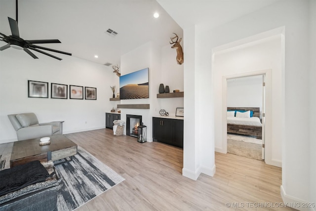living room featuring a ceiling fan, light wood-style floors, a glass covered fireplace, recessed lighting, and baseboards