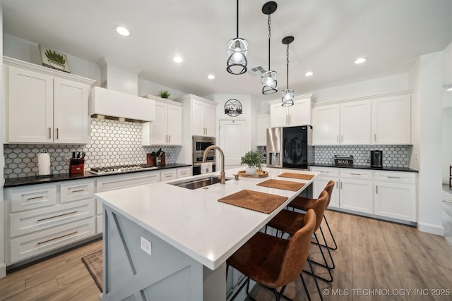 kitchen with stainless steel appliances, a sink, premium range hood, a kitchen breakfast bar, and white cabinets