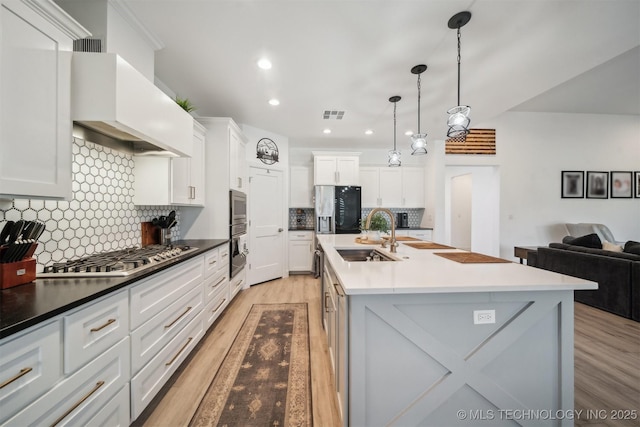 kitchen featuring appliances with stainless steel finishes, light wood finished floors, a sink, premium range hood, and backsplash