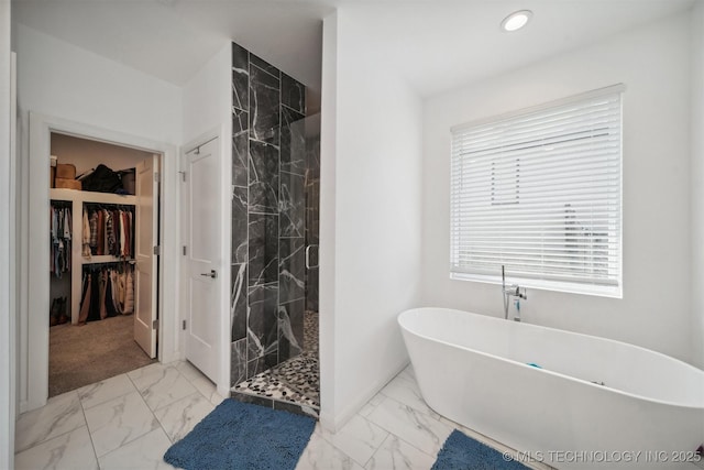 bathroom featuring marble look tile flooring, a marble finish shower, a walk in closet, a freestanding tub, and healthy amount of natural light