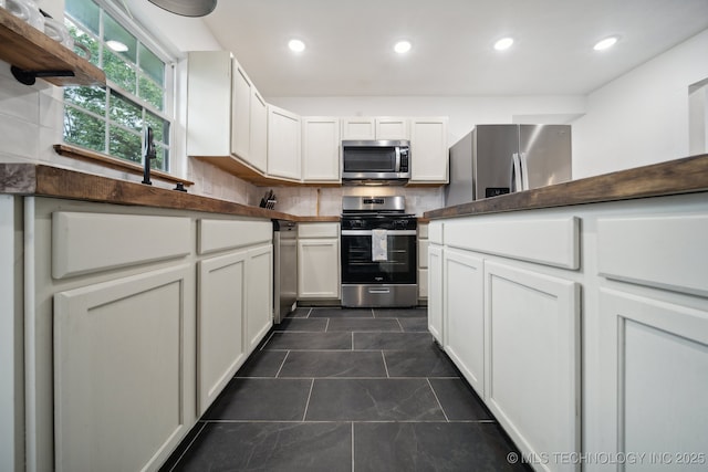 kitchen featuring stainless steel appliances, white cabinetry, dark tile patterned floors, backsplash, and recessed lighting