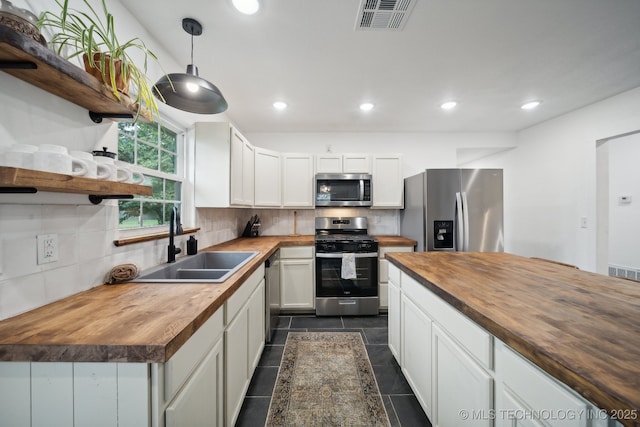 kitchen with butcher block counters, appliances with stainless steel finishes, a sink, open shelves, and decorative backsplash