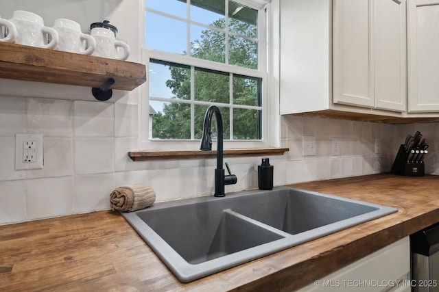 kitchen featuring wooden counters, a sink, white cabinetry, and tasteful backsplash