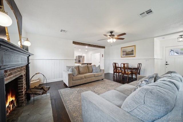living room with a ceiling fan, dark wood-style flooring, a wainscoted wall, and a fireplace