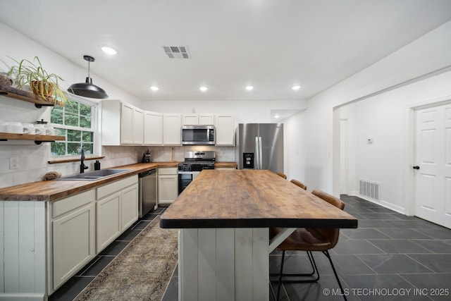 kitchen with butcher block countertops, stainless steel appliances, a sink, tasteful backsplash, and a center island
