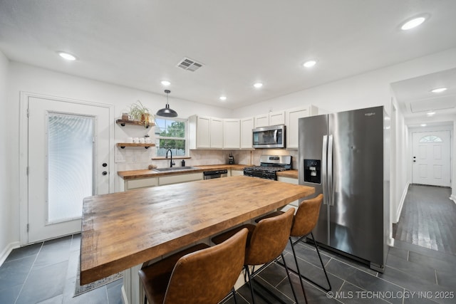 kitchen featuring appliances with stainless steel finishes, wood counters, a sink, white cabinetry, and recessed lighting