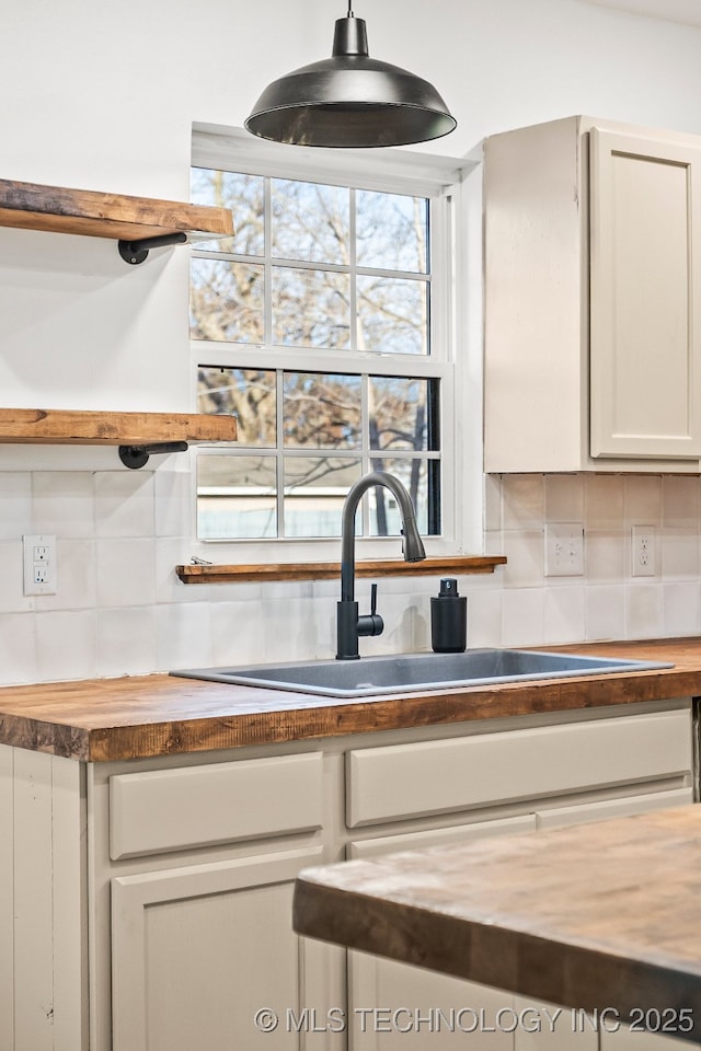 kitchen with butcher block counters, a sink, tasteful backsplash, and white cabinetry