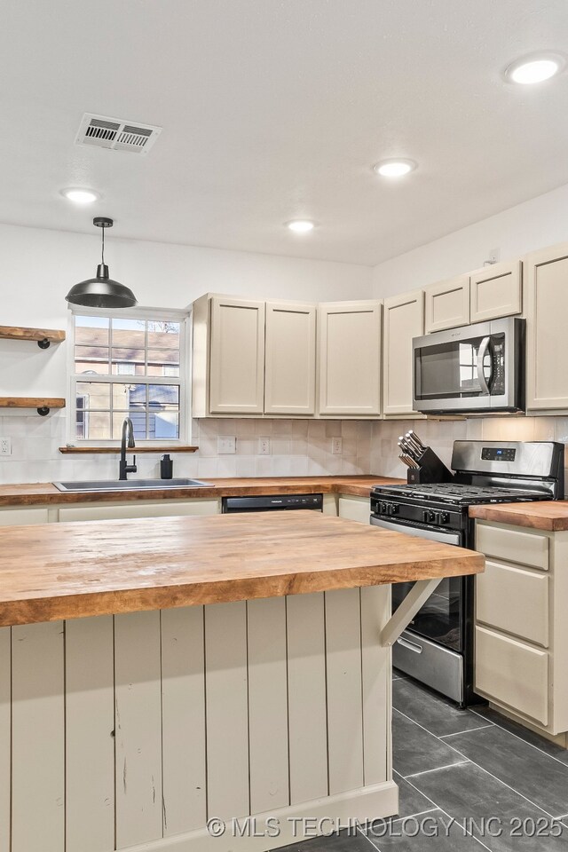 kitchen with wood counters, stainless steel appliances, a sink, decorative backsplash, and decorative light fixtures