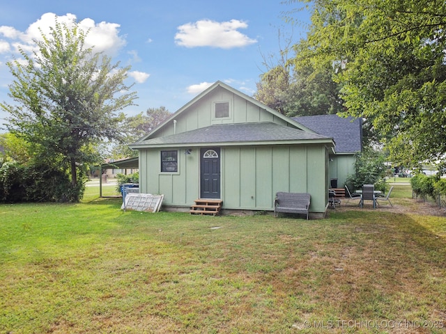 rear view of property with entry steps, board and batten siding, a shingled roof, and a lawn