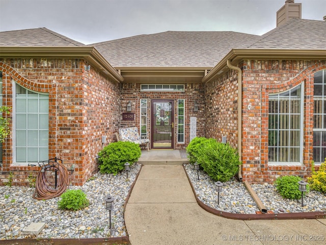 view of exterior entry with brick siding and a shingled roof