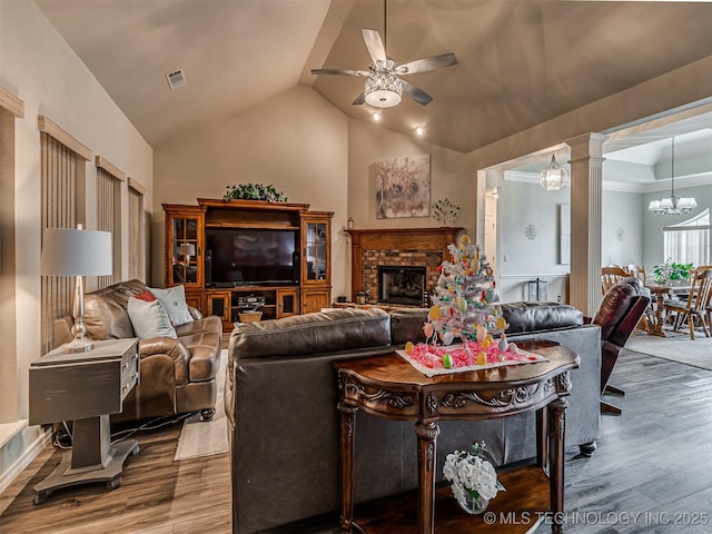 living area with a ceiling fan, wood finished floors, a chandelier, vaulted ceiling, and a fireplace