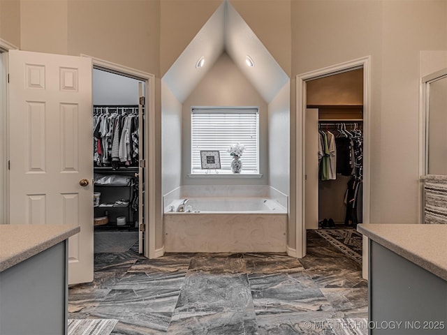 bathroom featuring marble finish flooring, a bath, a walk in closet, and lofted ceiling