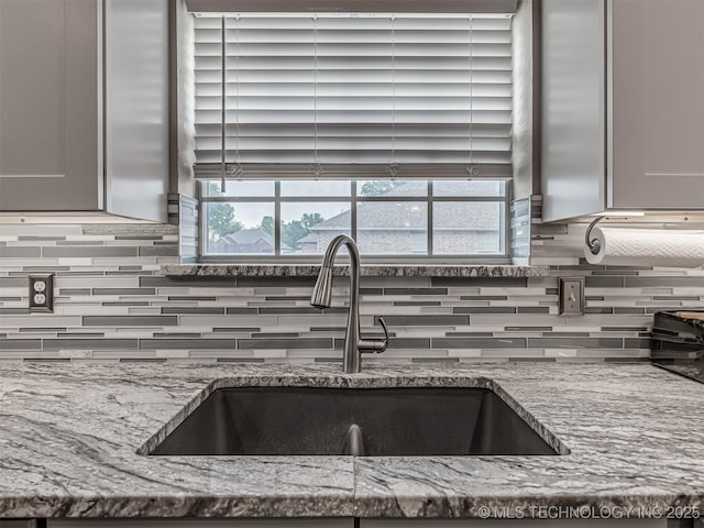 kitchen featuring a sink, backsplash, and light stone counters