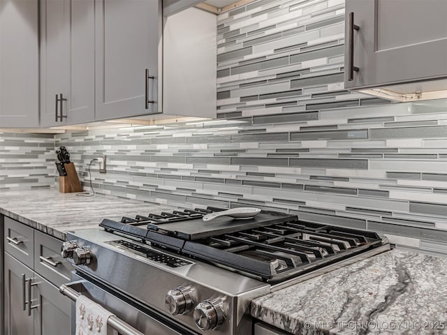 kitchen with stainless steel gas range, backsplash, gray cabinets, and light stone countertops