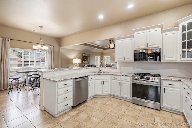 kitchen with appliances with stainless steel finishes, a peninsula, a sink, a chandelier, and white cabinets