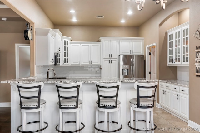 kitchen featuring stainless steel appliances, a peninsula, tasteful backsplash, white cabinets, and light stone countertops