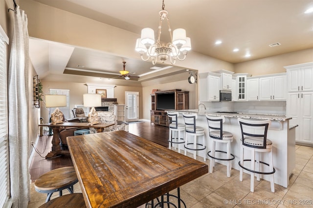 dining room with a fireplace, ceiling fan, a chandelier, a raised ceiling, and recessed lighting