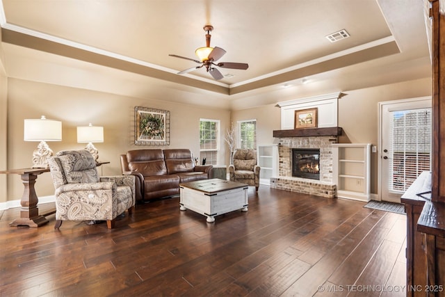 living area with a raised ceiling, ceiling fan, dark wood-style flooring, a fireplace, and ornamental molding