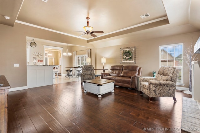 living area with a ceiling fan, a raised ceiling, dark wood-style floors, a chandelier, and crown molding