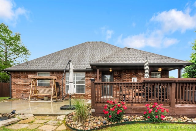 rear view of house featuring brick siding, roof with shingles, a deck, and a patio