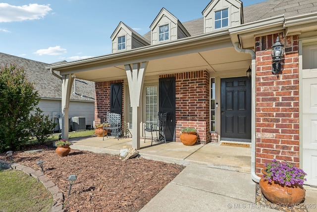 entrance to property featuring brick siding, covered porch, and a shingled roof