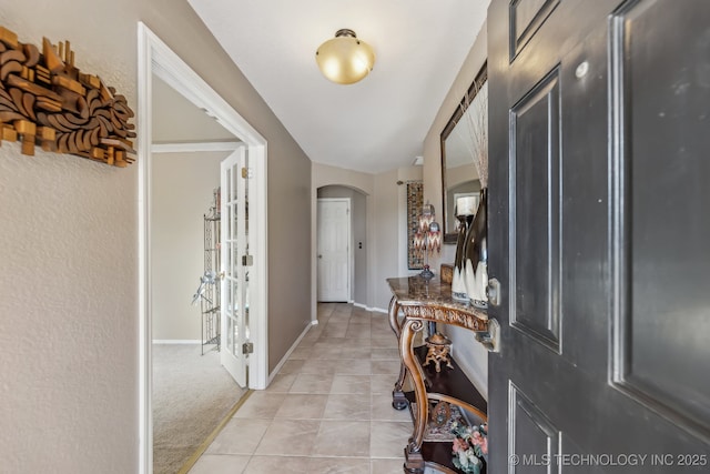 foyer entrance featuring arched walkways, baseboards, light tile patterned floors, and light carpet