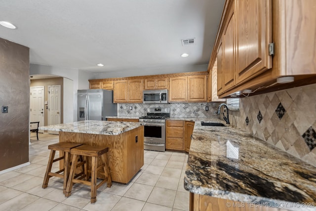 kitchen with appliances with stainless steel finishes, a sink, a center island, light stone countertops, and recessed lighting