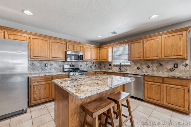 kitchen with appliances with stainless steel finishes, light tile patterned flooring, a breakfast bar area, a center island, and recessed lighting