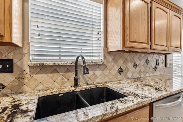kitchen featuring a sink, decorative backsplash, light stone countertops, light brown cabinetry, and dishwasher