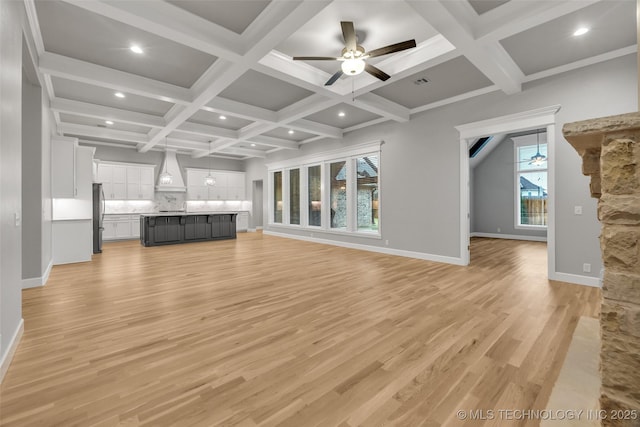 unfurnished living room with light wood finished floors, beam ceiling, coffered ceiling, a ceiling fan, and baseboards