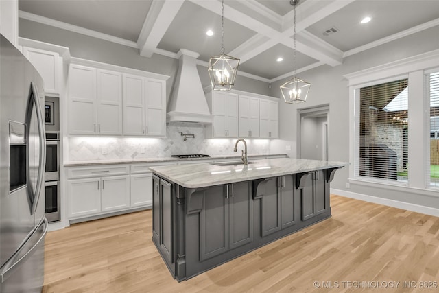 kitchen featuring a sink, stainless steel appliances, premium range hood, white cabinetry, and beam ceiling