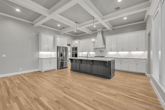 kitchen featuring stainless steel appliances, wall chimney exhaust hood, white cabinetry, light countertops, and beam ceiling
