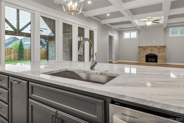 kitchen with a sink, stainless steel dishwasher, coffered ceiling, gray cabinets, and light stone counters