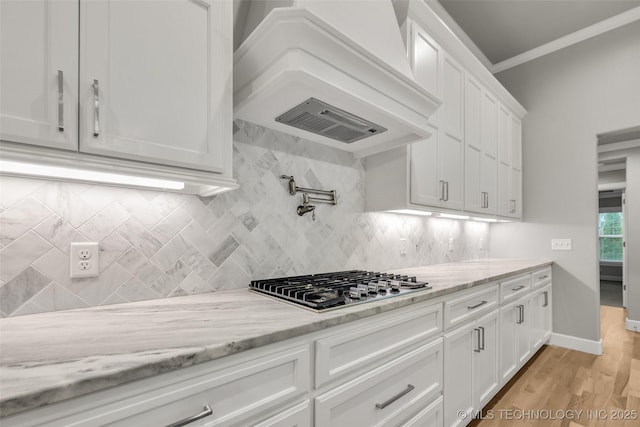 kitchen featuring stainless steel gas cooktop, white cabinetry, tasteful backsplash, light stone counters, and ornamental molding