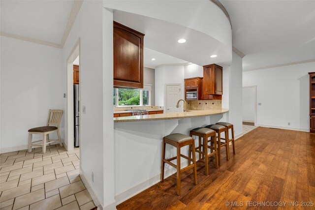 9304 E 113th St S, Bixby, OK 74008 - kitchen featuring crown molding, tasteful backsplash, light countertops, stainless steel appliances, and a kitchen breakfast bar