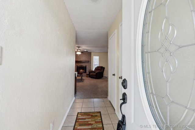 hallway featuring light tile patterned floors, light colored carpet, a textured ceiling, and baseboards