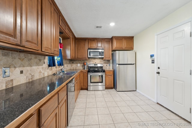 kitchen with appliances with stainless steel finishes, a sink, brown cabinetry, backsplash, and light tile patterned floors
