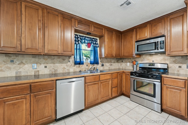 kitchen featuring appliances with stainless steel finishes, a sink, brown cabinetry, and a textured ceiling