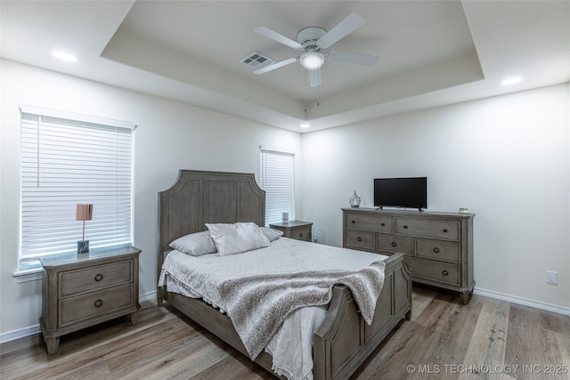 bedroom featuring a raised ceiling, light wood-style flooring, baseboards, recessed lighting, and ceiling fan