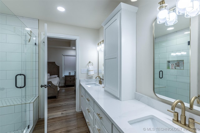 ensuite bathroom with double vanity, a shower stall, wood finished floors, and recessed lighting