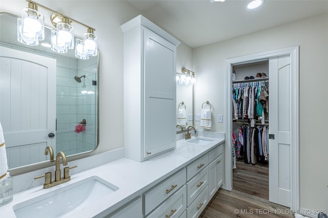 bathroom featuring wood finished floors, tiled shower, double vanity, recessed lighting, and a spacious closet