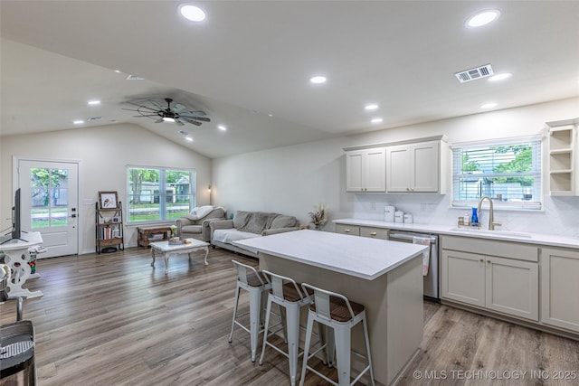 kitchen featuring a sink, stainless steel dishwasher, a center island, wood finished floors, and a breakfast bar