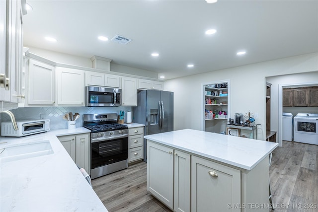 kitchen featuring appliances with stainless steel finishes, independent washer and dryer, light wood-style floors, a kitchen island, and decorative backsplash
