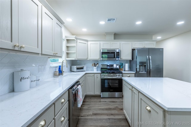 kitchen with stainless steel appliances, a sink, open shelves, wood finished floors, and backsplash