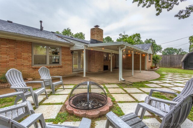 back of house with a fire pit, a patio area, a chimney, brick siding, and fence